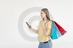 Portrait of a pretty woman holding shopping bags while using mobile phone isolated over white background