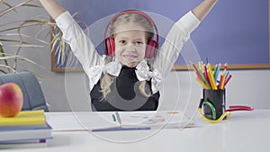 Portrait of pretty caucasian girl putting on earphones, making victory gesture and shaking head. Happy cheerful child