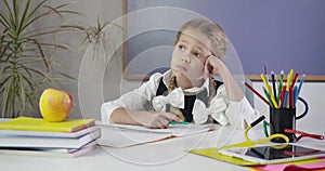 Portrait of pretty Caucasian girl sitting writing in exercise book and looking away thoughtfully. Elementary student