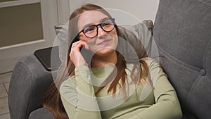 Portrait of pretty caucasian woman in glasses talking on phone. Happy smiling woman talking with friends lying on couch