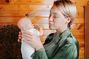 Portrait of pretty caucasian young woman holding newborn baby doll in arms and looking at her while standing indoors.