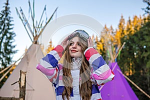 Portrait of Pretty Caucasian young woman Near The Indian Tipi or Wigwam in ski outfit and Winter Sports Mask on her Head