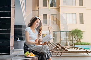 Portrait of pretty cheerful woman relax and reading book in vacation on summer season at resort swimming pool