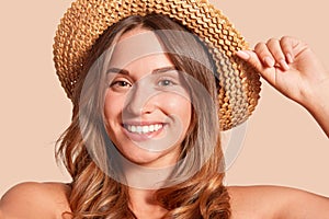 Portrait of pretty cheerful woman wearing straw hat, attractive female looking smiling directly at camera, expresses happyness,