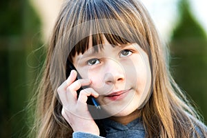 Portrait of pretty child girl with long hair talking on cell phone. Little female kid communicating using smartphone. Children