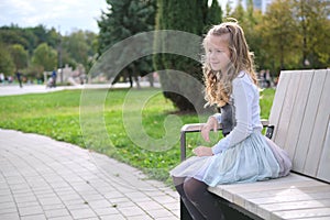 Portrait of pretty child girl sitting on park bench outdoors