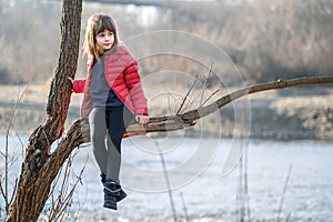 Portrait of a pretty child girl sitting on a tree branch in autumn outdoors