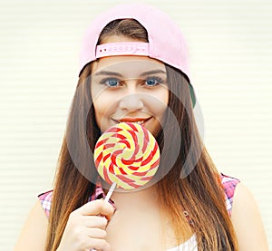 Portrait pretty cool young girl wearing a pink baseball cap with sweet caramel lollipop