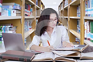 Pretty female student doing schoolwork in library photo