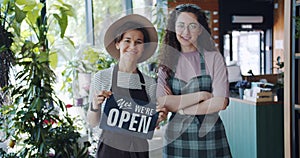 Portrait of pretty florists in flower store with open sign starting business