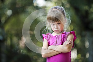 Portrait of pretty funny moody young blond child girl in pink sleeveless dress looks in camera feeling angry and unsatisfied on b