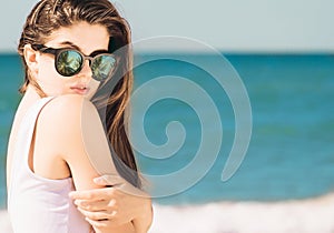 Portrait of a pretty girl with long hair in trendy sunglasses with palms reflection posing on the beach