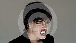 Portrait of pretty girl shouting. Young brunette woman with red lips screaming isolated on grey background. Concept of