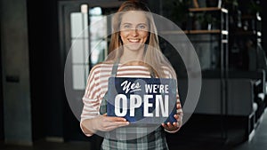 Portrait of pretty girl standing in cafe holding open sign welcoming customers