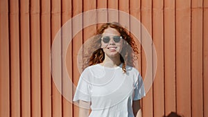 Portrait of pretty girl teenager in sunglasses standing outdoors against wall