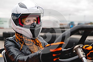 Portrait of a pretty girl wearing a white helmet close up, detail of Go-kart. karting track racing, copy space. serious look,