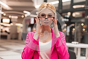 Portrait pretty glamorous business young woman in fashionable pink jacket with trendy hairstyle posing in cafe. Modern elegant