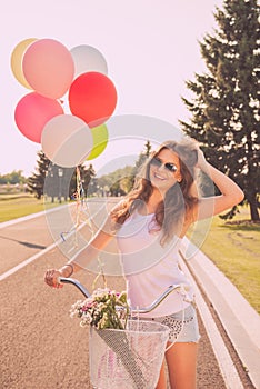Portrait of pretty happy woman in glasses with bicycle and balloons