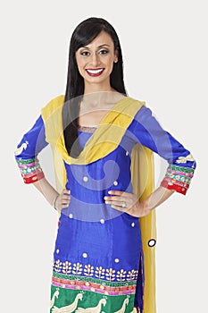 Portrait of pretty Indian woman in traditional wear standing with hands on hips over gray background