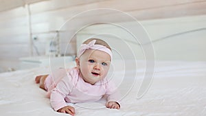 Portrait of pretty infant in pink dress on a bed at home