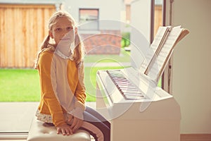 Portrait of pretty little girl having piano lesson at modern white e-piano