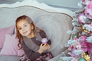 Portrait of Pretty little girl holds a Christmas toy at hand on a sofa near Christmas tree