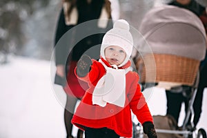 Portrait of pretty little girl in red coat enjoying winter day. In the background, her family, mom, dad and little