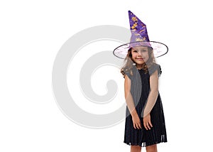 Portrait of pretty little girl wearing a wizard hat and dressed in stylish carnival dress, looking at camera posing with crossed