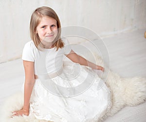 Portrait of pretty little girl in white dress , looking at camera and smiling, standing against gray background