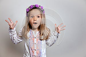 Portrait of pretty little girl in white dress and purple wreath on gray isolated background.