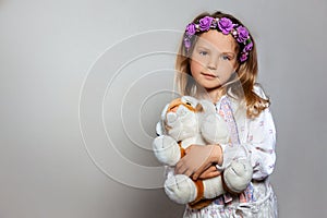 Portrait of pretty little girl  in white dress and purple wreath with plush tiger toy on gray isolated background.