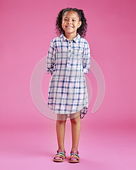 A portrait of a pretty little mixed race girl with curly hair posing against a pink copyspace background in a studio. A