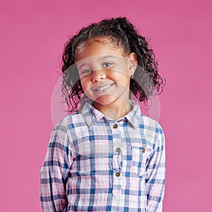 A portrait of a pretty little mixed race girl with curly hair posing against a pink copyspace background in a studio. A