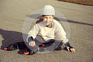 Portrait of pretty little teenager child girl sitting in white helmet, inline skates and safety equipment