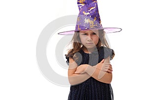 Portrait of pretty little witch angry upset girl wearing a wizard hat and dressed in stylish carnival dress, looking at camera