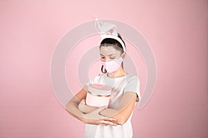 Portrait of a pretty lovely woman wearing bunny ears standing isolated over pink background and hugging gift box. Easter during