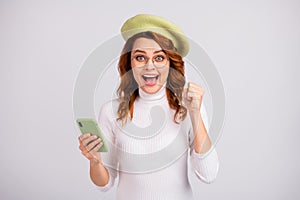 Portrait of pretty lucky cheerful wavy-haired girl blogger using cell having fun rejoicing isolated over light gray