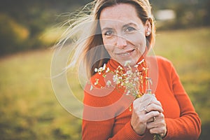 Portrait of a pretty middle-aged  woman outside in a park, picking flowers