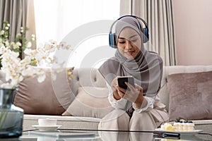 Portrait of pretty Muslim lady in hijab and headset listening to music at home. asian woman in Arab scarf enjoying