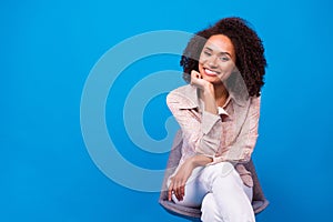Portrait of pretty positive girl sit chair hand touch chin toothy smile empty space  on blue color background