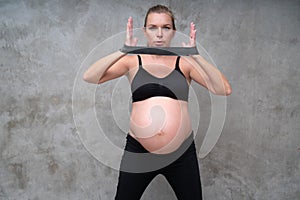 Portrait of pretty pregnant woman exercises with resistance band in the gym