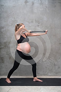 Portrait of pretty pregnant woman exercises with resistance band in the gym