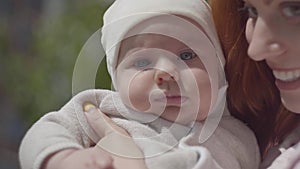 Portrait pretty red-haired woman holding the baby in arms and smiling in the yard close-up. The lady enjoying the sunny