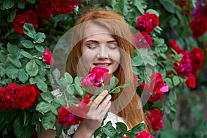 Portrait of a pretty redhead girl dressed in a white light dress on a background of blooming roses. Outdoor