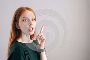 Portrait of pretty redhead young woman model pointing up with finger looking at camera on white background.