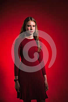 Portrait pretty sad teen girl in stylish red dress over red background looking at camera