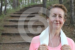 Portrait of pretty senior woman listening to music after running. Training outdoors in the morning