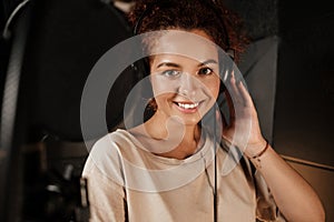 Portrait of pretty singer in headphones happily looking in camera in modern recording studio