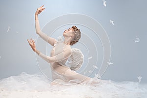 Portrait of pretty, slim beautiful young girl, graceful ballerina in image of angel with wings sitting on cloud 