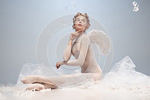 Portrait of pretty, slim beautiful young girl, graceful ballerina in image of angel with wings sitting on cloud 